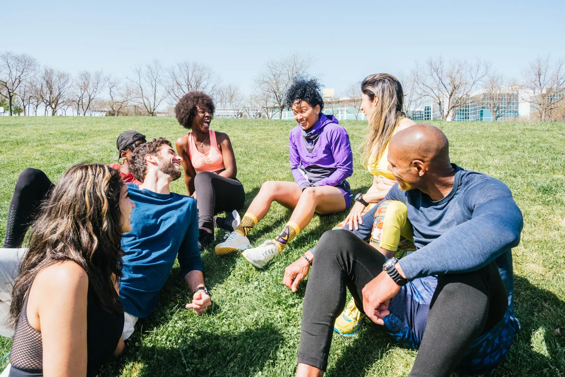 A therapy group seated in a circle outdoors on a sunny day, with supportive engagement between participants